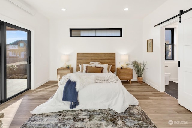 bedroom featuring light hardwood / wood-style floors, access to exterior, ensuite bathroom, and a barn door