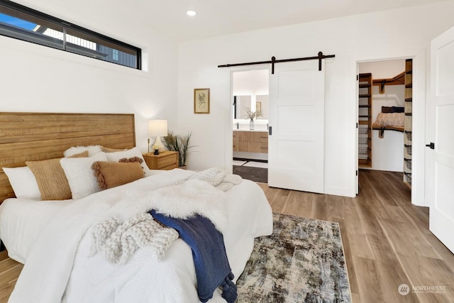 bedroom with a walk in closet, a closet, light wood-type flooring, ensuite bathroom, and a barn door