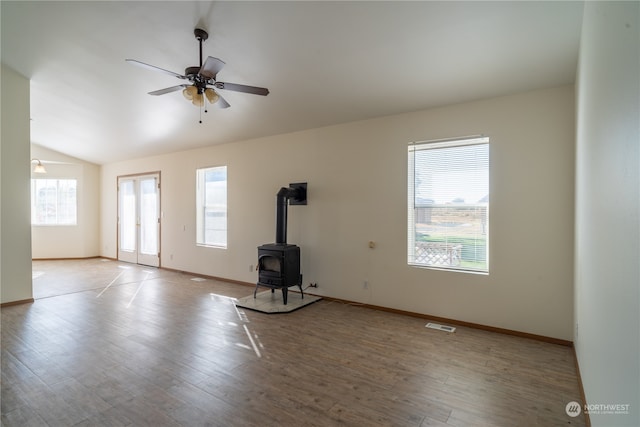 unfurnished living room featuring ceiling fan, vaulted ceiling, a wood stove, and light wood-type flooring