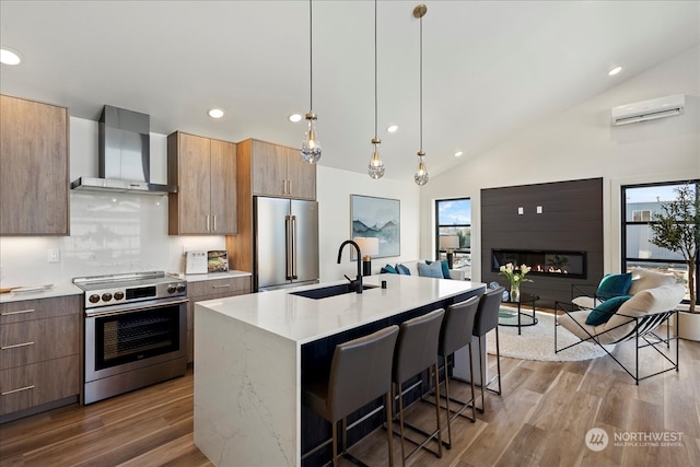 kitchen featuring an island with sink, dark hardwood / wood-style floors, wall chimney range hood, a breakfast bar area, and appliances with stainless steel finishes