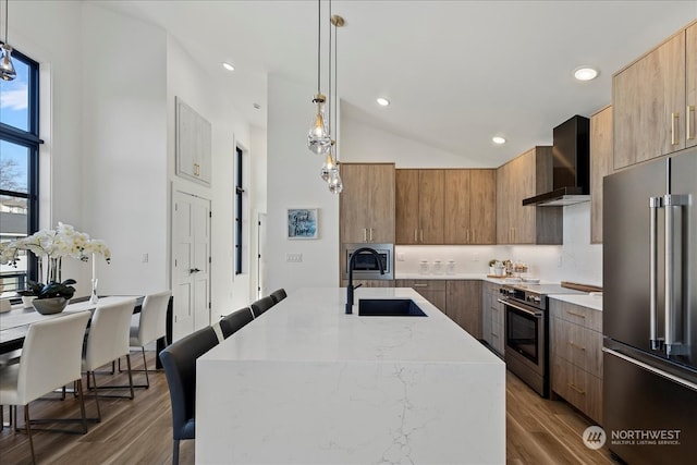 kitchen featuring sink, decorative light fixtures, a center island with sink, wall chimney range hood, and high quality appliances