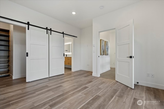 unfurnished bedroom featuring light wood-type flooring, a barn door, and connected bathroom