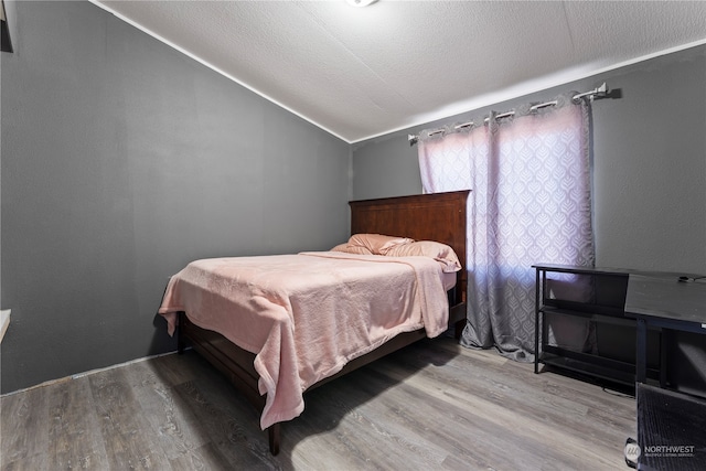 bedroom featuring hardwood / wood-style flooring, lofted ceiling, and a textured ceiling