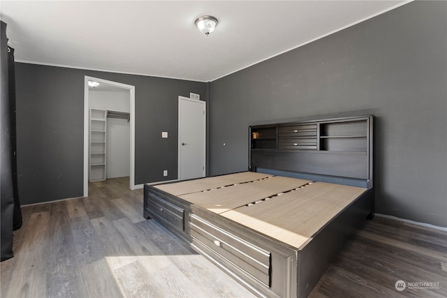 bedroom featuring a spacious closet, crown molding, a closet, and wood-type flooring