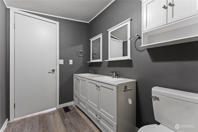 bathroom with vanity, wood-type flooring, crown molding, toilet, and a textured ceiling