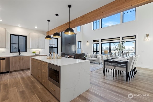 kitchen with built in microwave, sink, dishwasher, a kitchen island, and light stone countertops