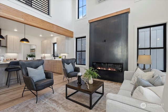 living room with a high ceiling, a large fireplace, sink, and light wood-type flooring