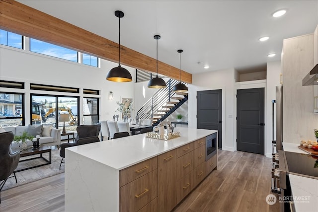 kitchen featuring pendant lighting, a center island, stainless steel microwave, beamed ceiling, and hardwood / wood-style floors