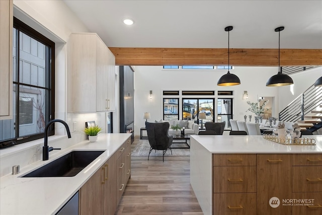 kitchen featuring sink, light hardwood / wood-style flooring, hanging light fixtures, beam ceiling, and light stone countertops