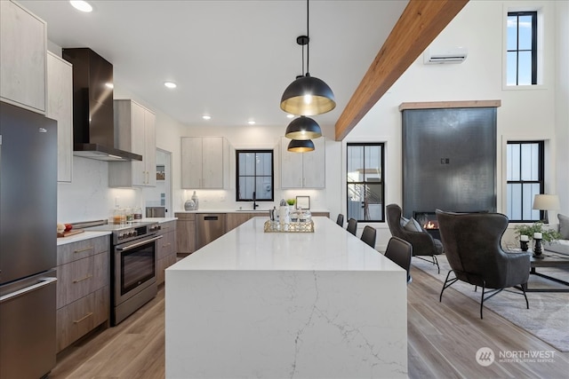 kitchen with wall chimney exhaust hood, decorative light fixtures, a center island, light wood-type flooring, and stainless steel appliances