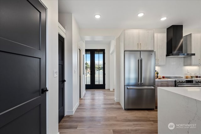 kitchen with wall chimney range hood, hardwood / wood-style flooring, appliances with stainless steel finishes, backsplash, and french doors