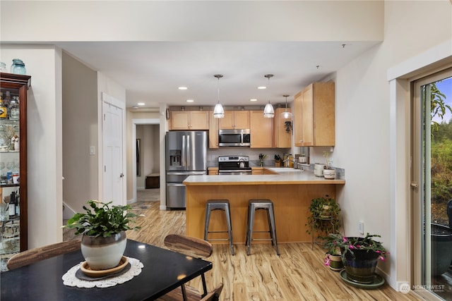 kitchen featuring appliances with stainless steel finishes, kitchen peninsula, light hardwood / wood-style floors, and light brown cabinets