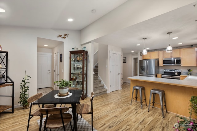 kitchen featuring light hardwood / wood-style flooring, light brown cabinetry, kitchen peninsula, stainless steel appliances, and a breakfast bar