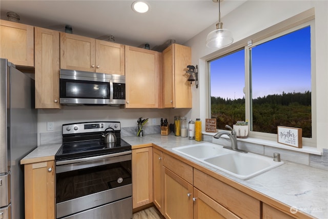 kitchen featuring appliances with stainless steel finishes, sink, light brown cabinets, and decorative light fixtures