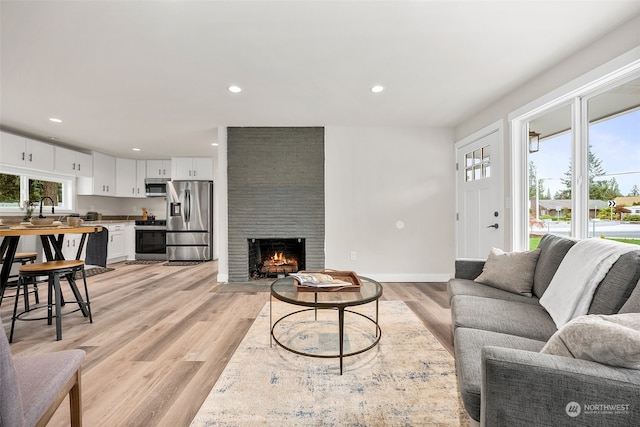 living room with sink, a wealth of natural light, a large fireplace, and light hardwood / wood-style flooring