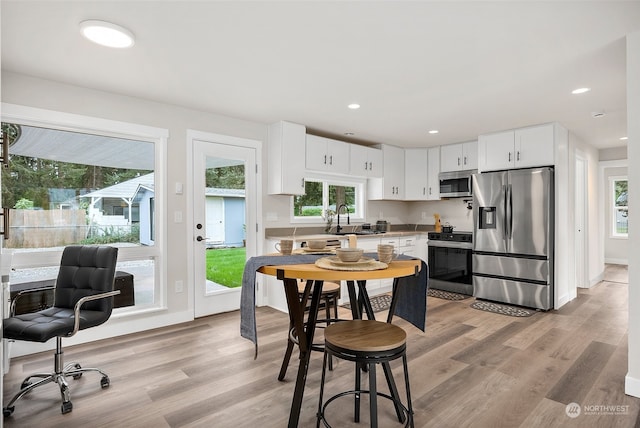 kitchen with plenty of natural light, white cabinets, appliances with stainless steel finishes, and light wood-type flooring