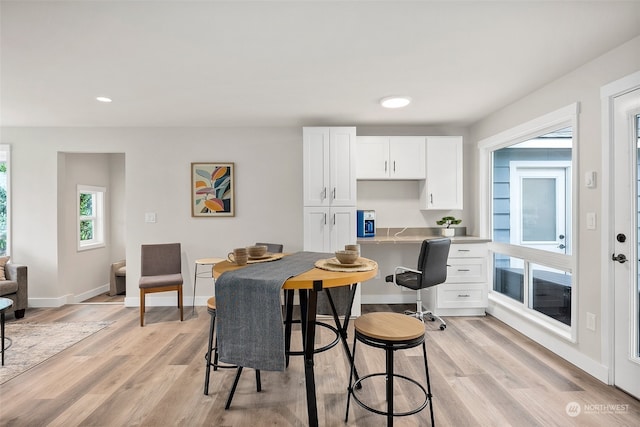 kitchen with built in desk, white cabinetry, a breakfast bar, and light hardwood / wood-style flooring