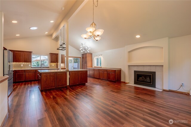 kitchen with stainless steel fridge, dark hardwood / wood-style flooring, a tiled fireplace, vaulted ceiling, and decorative light fixtures