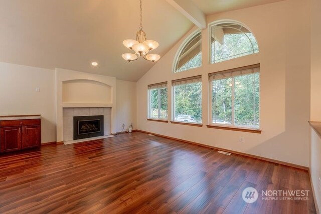 unfurnished living room featuring a tiled fireplace, plenty of natural light, a chandelier, and dark hardwood / wood-style flooring