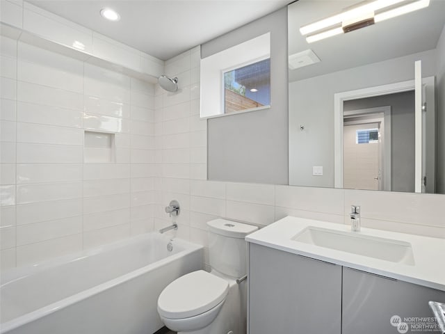 full bathroom with toilet, tasteful backsplash, tile walls, tiled shower / bath combo, and vanity