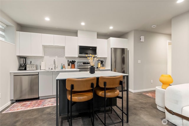 kitchen featuring light countertops, decorative backsplash, appliances with stainless steel finishes, white cabinets, and a kitchen island