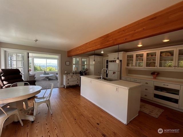 kitchen featuring light wood-type flooring, white cabinets, sink, hanging light fixtures, and a center island with sink