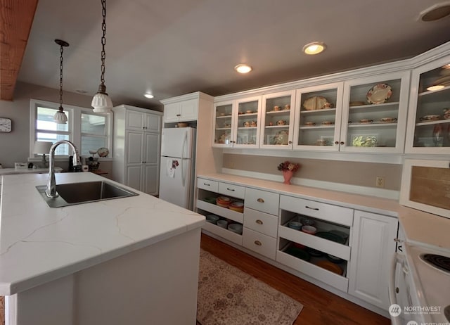 kitchen with white appliances, sink, dark hardwood / wood-style flooring, hanging light fixtures, and a center island with sink