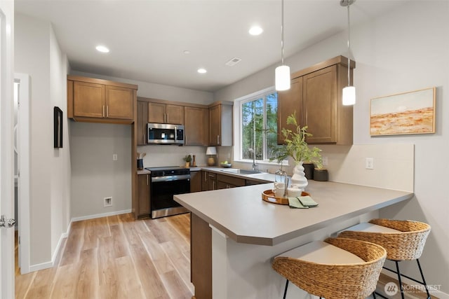 kitchen with a peninsula, electric range, a sink, brown cabinetry, and stainless steel microwave