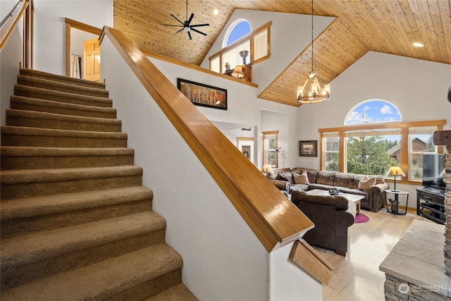 stairway with high vaulted ceiling, ceiling fan with notable chandelier, wood ceiling, and wood finished floors