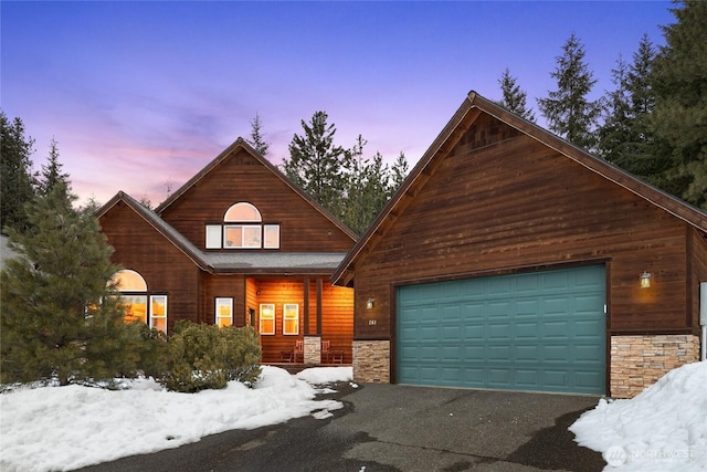 view of front of house featuring aphalt driveway, stone siding, covered porch, and a garage