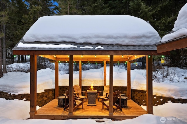 snow covered patio with an outdoor fire pit and a deck