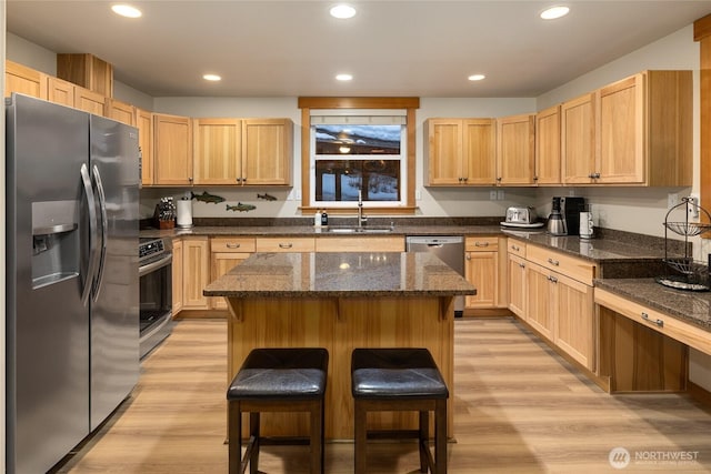 kitchen featuring a breakfast bar, a center island, stainless steel appliances, a sink, and dark stone countertops