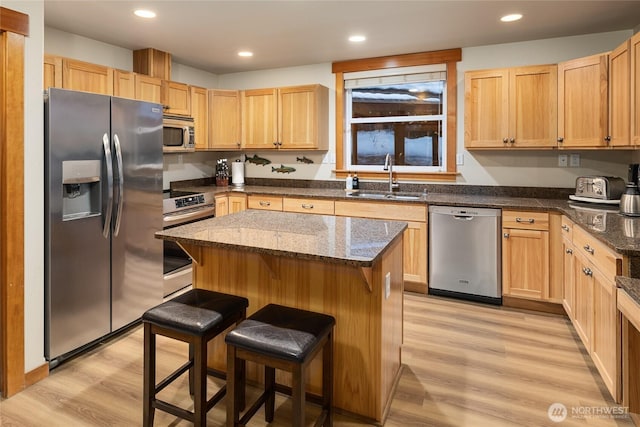 kitchen featuring dark stone counters, a kitchen island, a kitchen breakfast bar, stainless steel appliances, and a sink