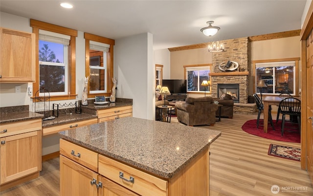 kitchen featuring stone countertops, light brown cabinets, a fireplace, a center island, and light wood finished floors