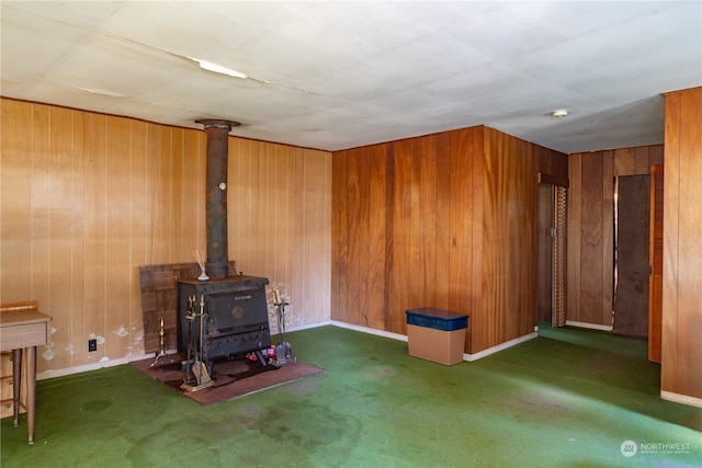 unfurnished living room with a wood stove, wooden walls, and dark carpet