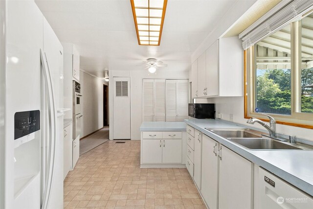 kitchen with white appliances, a sink, ceiling fan, white cabinets, and light countertops