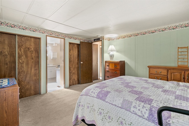 bedroom featuring light carpet, wood walls, and ensuite bathroom