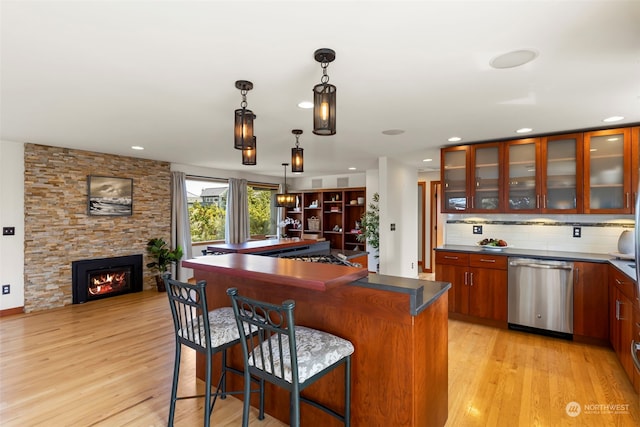 bar featuring pendant lighting, stainless steel dishwasher, light hardwood / wood-style flooring, a fireplace, and decorative backsplash