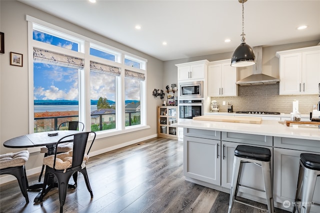 kitchen with decorative backsplash, white cabinetry, wall chimney exhaust hood, and appliances with stainless steel finishes