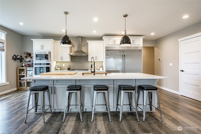 kitchen featuring white cabinets, built in appliances, a spacious island, and wall chimney range hood