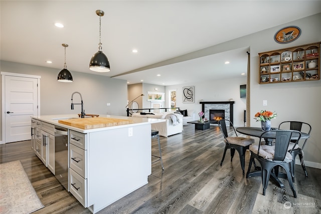 kitchen with sink, dark wood-type flooring, an island with sink, decorative light fixtures, and a fireplace