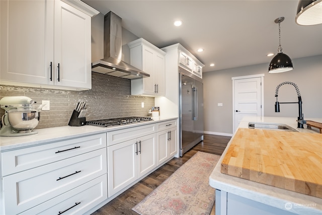 kitchen featuring appliances with stainless steel finishes, wall chimney exhaust hood, sink, butcher block countertops, and white cabinetry