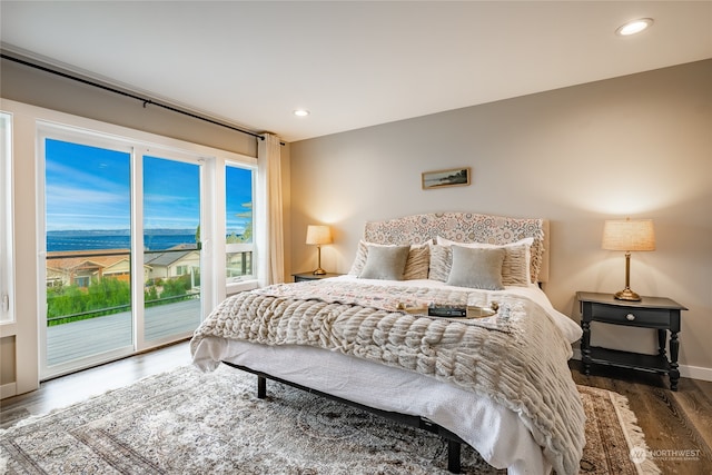 bedroom with dark hardwood / wood-style flooring, access to outside, and a water view