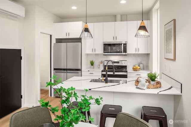 kitchen featuring decorative light fixtures, a wall unit AC, stainless steel appliances, and white cabinets