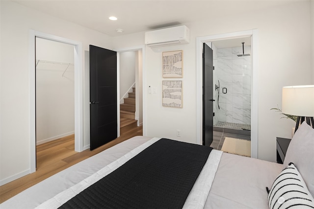 bedroom with connected bathroom, a closet, a wall mounted AC, and light hardwood / wood-style floors