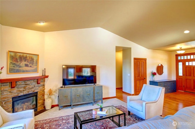 living room featuring vaulted ceiling, a fireplace, and light wood-type flooring