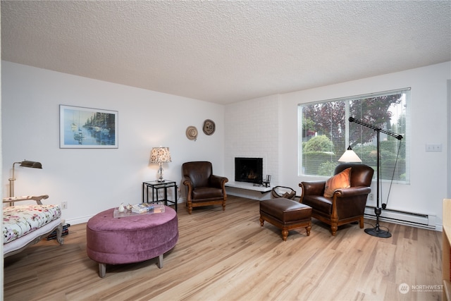 living room with light wood-type flooring, a brick fireplace, a baseboard heating unit, and a textured ceiling