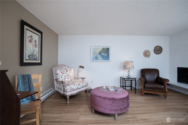 sitting room featuring a textured ceiling, light wood-type flooring, a fireplace, and baseboard heating