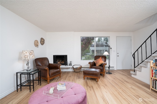 living room with a brick fireplace, a baseboard heating unit, wood-type flooring, and a textured ceiling