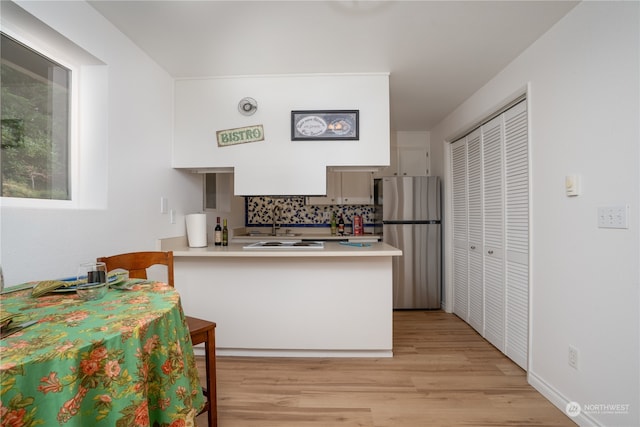 kitchen with decorative backsplash, white cabinets, stainless steel refrigerator, kitchen peninsula, and light hardwood / wood-style flooring